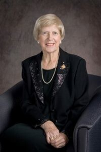 Portrait of Lois Else Hole. She wears all black, including black blazer with a pearl necklace.